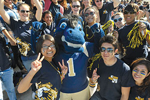 The school mascot Gunrock celebrates with a group of students during homecoming at Aggie Stadium